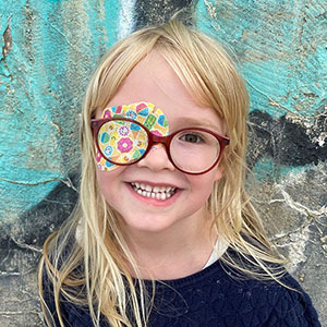 Glad tjej med glasögon och Ortopad ögonplåster.. Ett av många glasögonbarn.